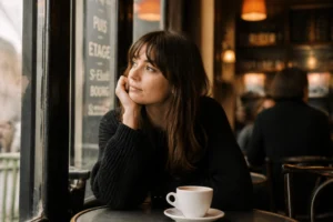 Femme pensive assise seule dans un café, regardant par la fenêtre, lumière naturelle douce