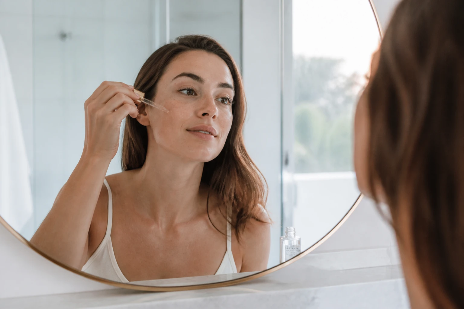 Femme appliquant un sérum à l'acide glycolique sur son visage devant un miroir