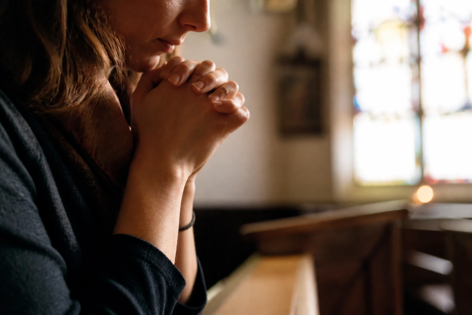 Femme priant dans une église, mains jointes, lumière douce d'un vitrail