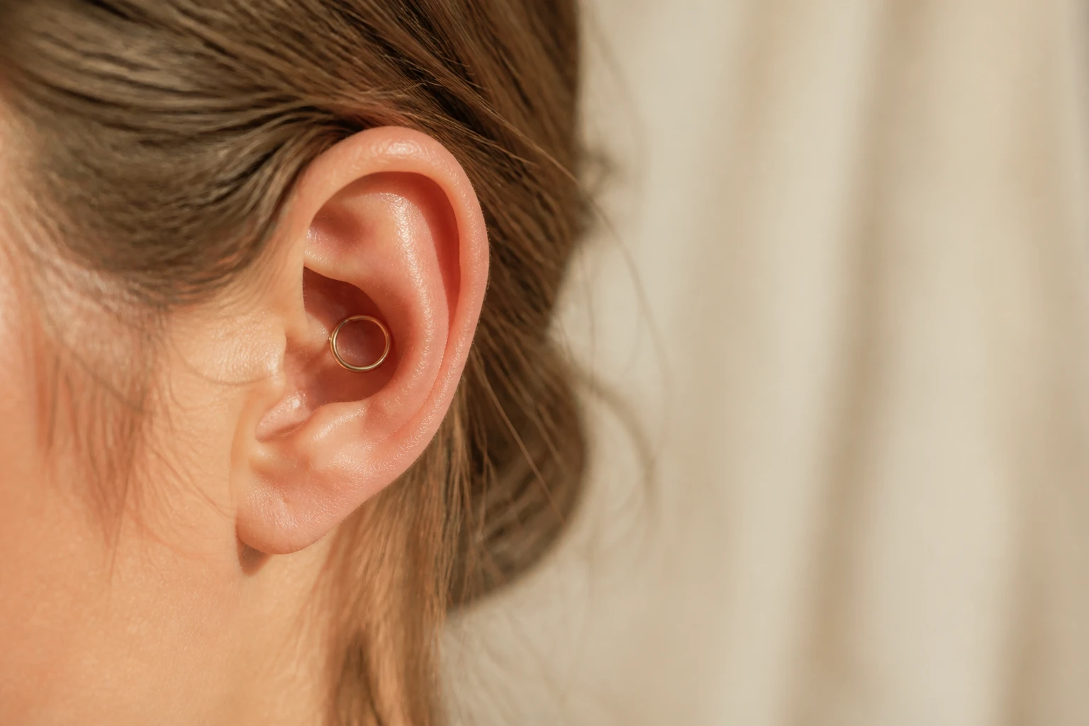 Gros plan d'une oreille avec un piercing conch et un anneau doré