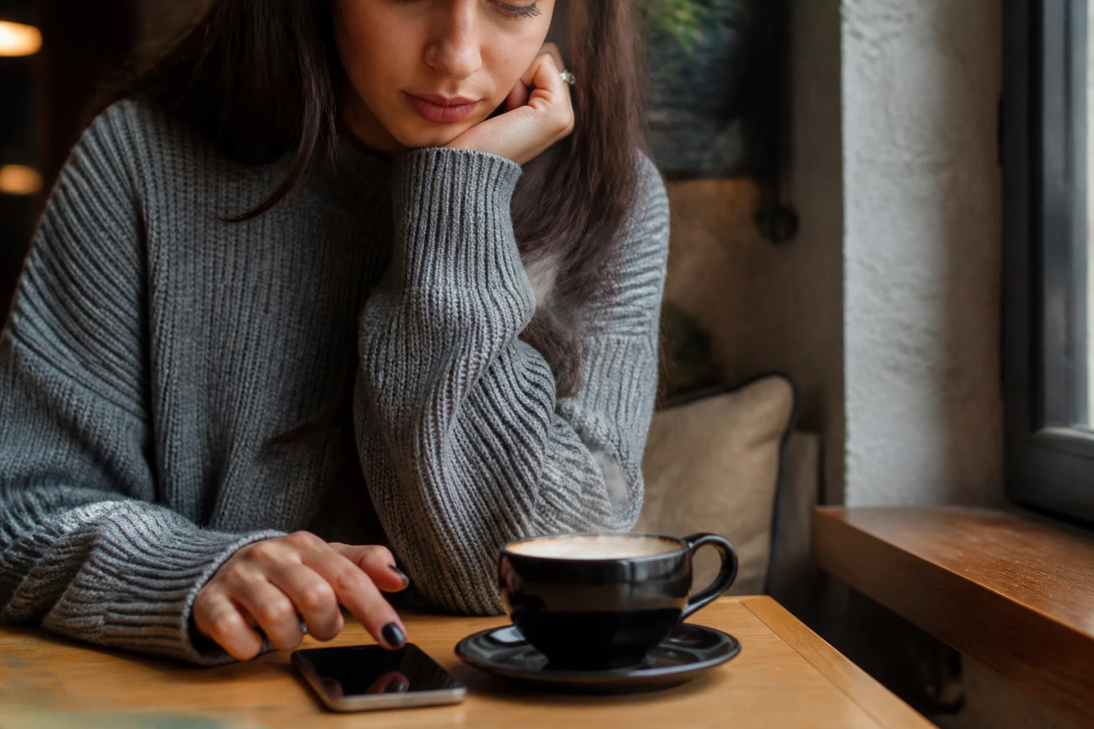 Jeune femme pensive dans un café regardant son téléphone, doute amoureux
