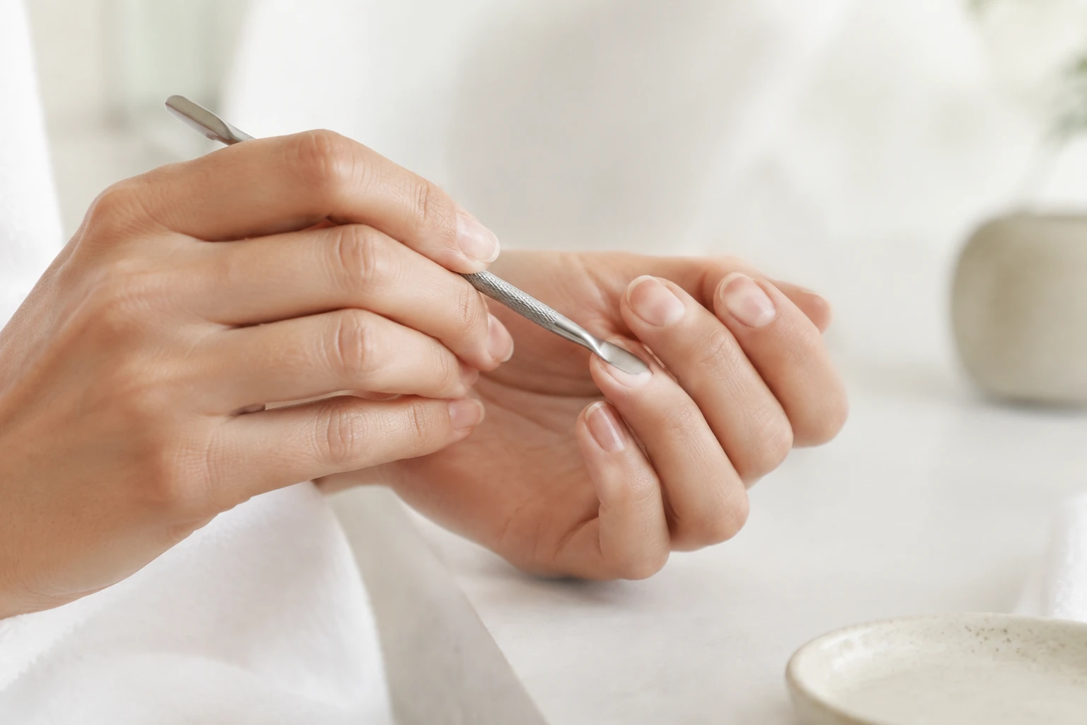 Femme utilisant un repousse-cuticules en inox pour repousser délicatement les cuticules de ses ongles